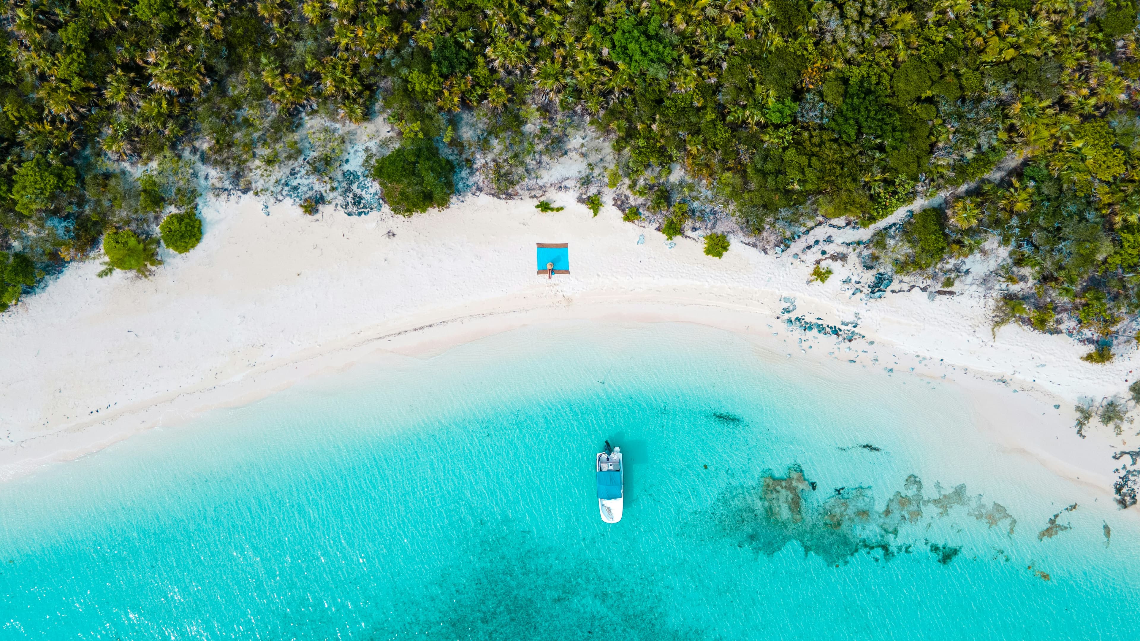 A boat anchored off a white sand beach in the Bahamas, from above